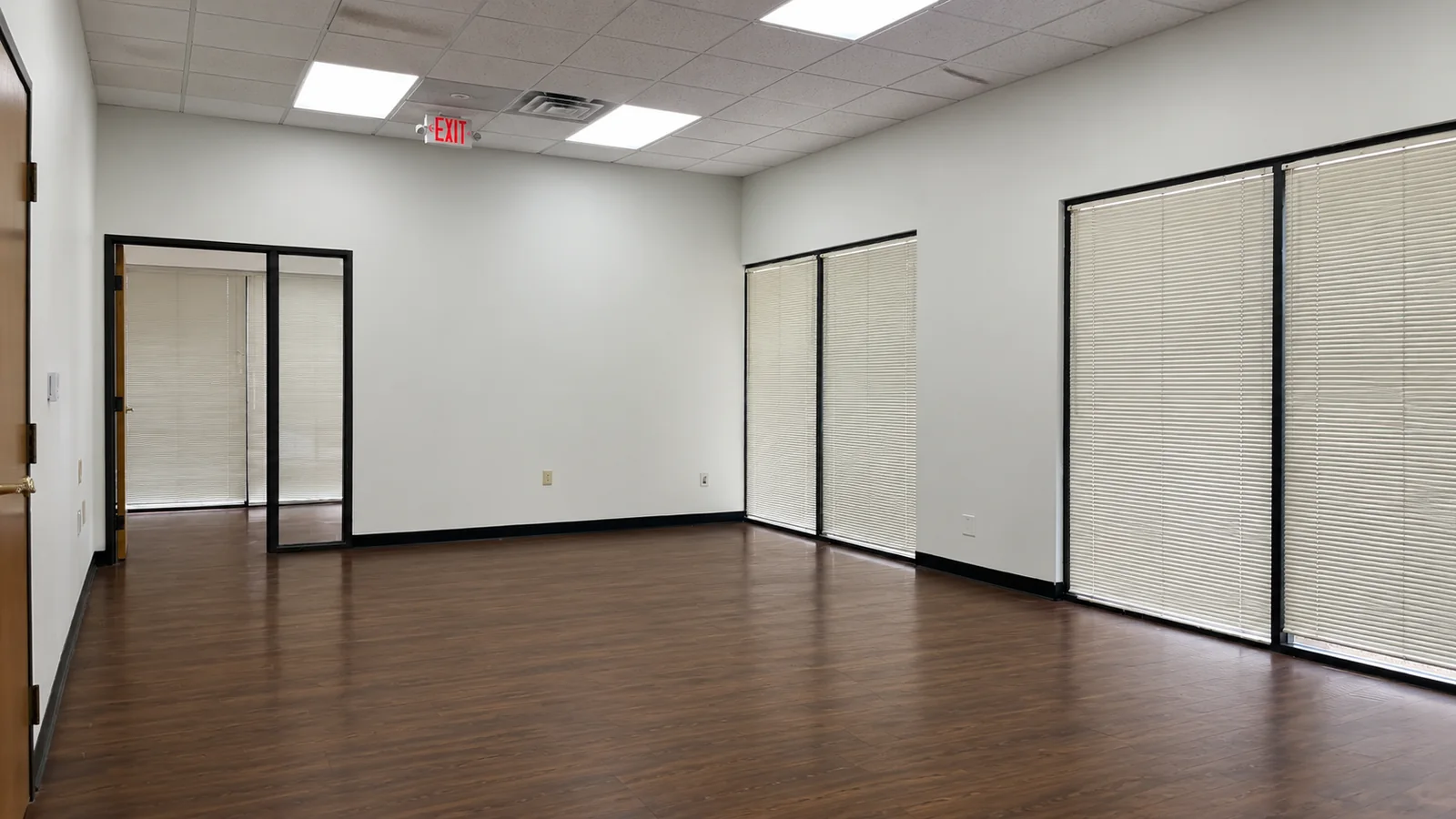 Open room inside Suite 100B with fresh white paint, LED panel lights and windows along one wall